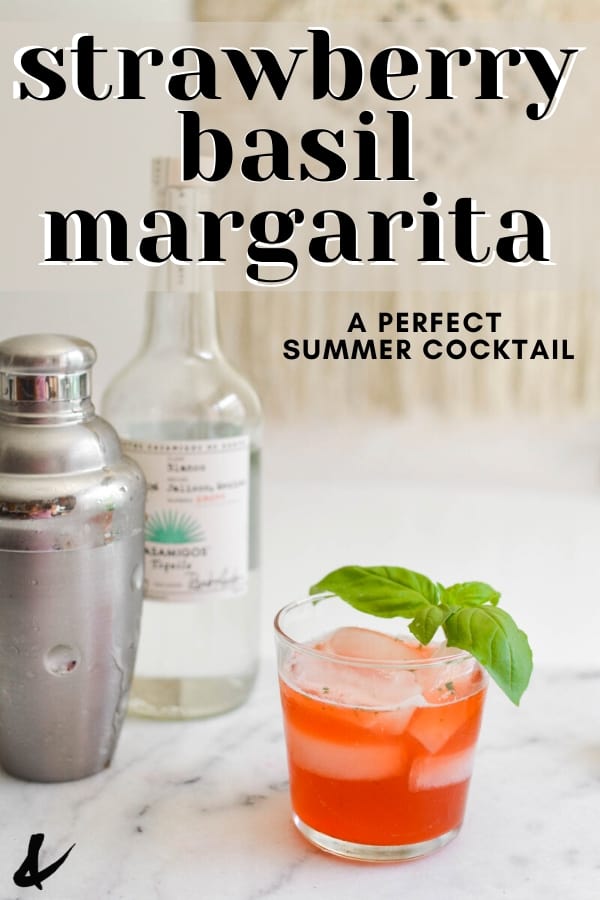 A strawberry basil margarita on a table next to a cocktail shaker and bottle of tequila with text overlay.