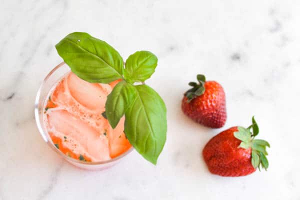 a pink Strawberry Margarita with a basil garnish on a table next to a few strawberries