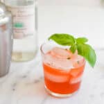 A close up of a glass of cocktail with basil garnish.