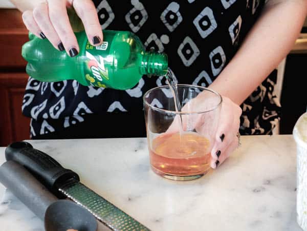 Woman pouring 7UP into a short cocktail glass on the counter. 