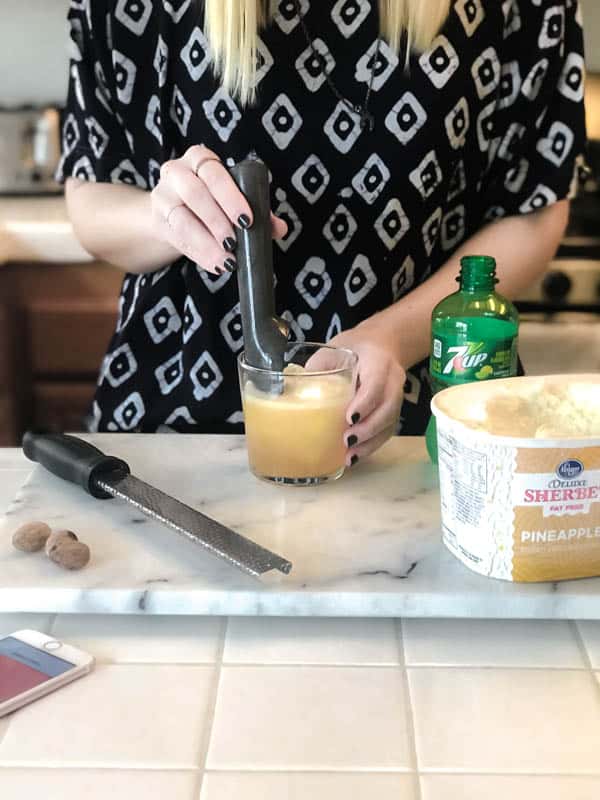 Woman adding a scoop of pineapple sherbet to a short cocktail glass with rum on a counter. 