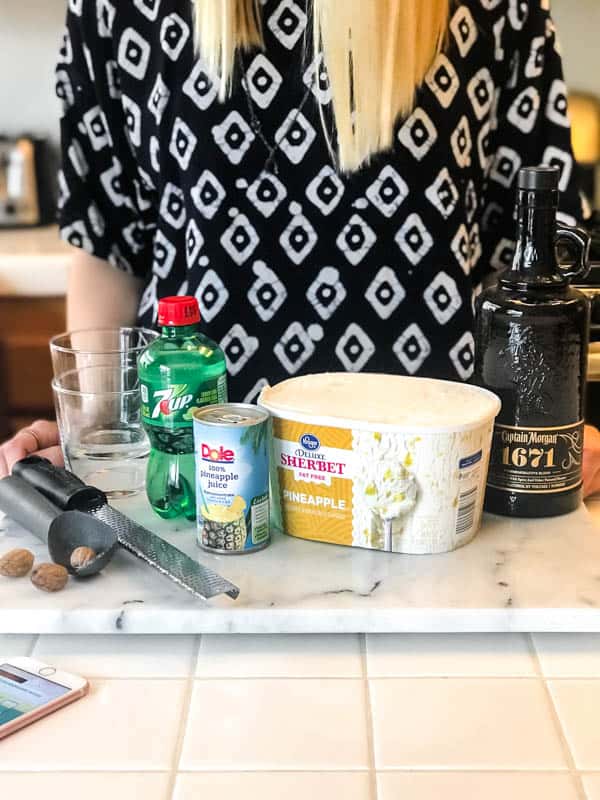 Ingredients to make a Spiced Rum Pineapple Float on a counter with a woman standing behind it.