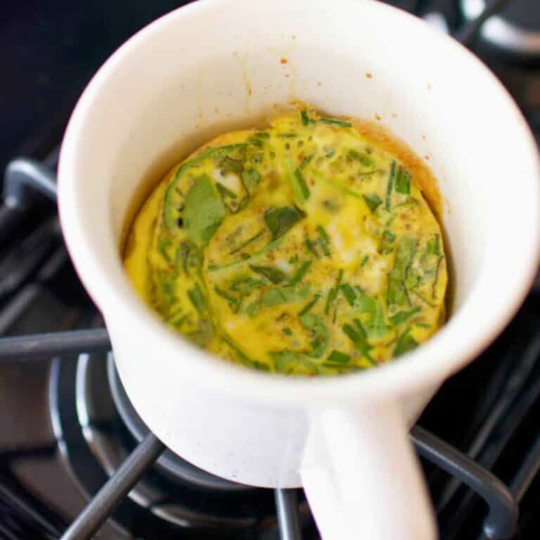 A white mug with baked eggs and herbs in it.