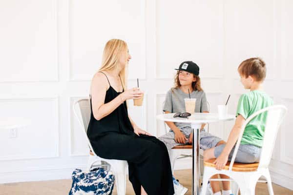 Mom holding a coffee drink and sitting at a table with two sons. 