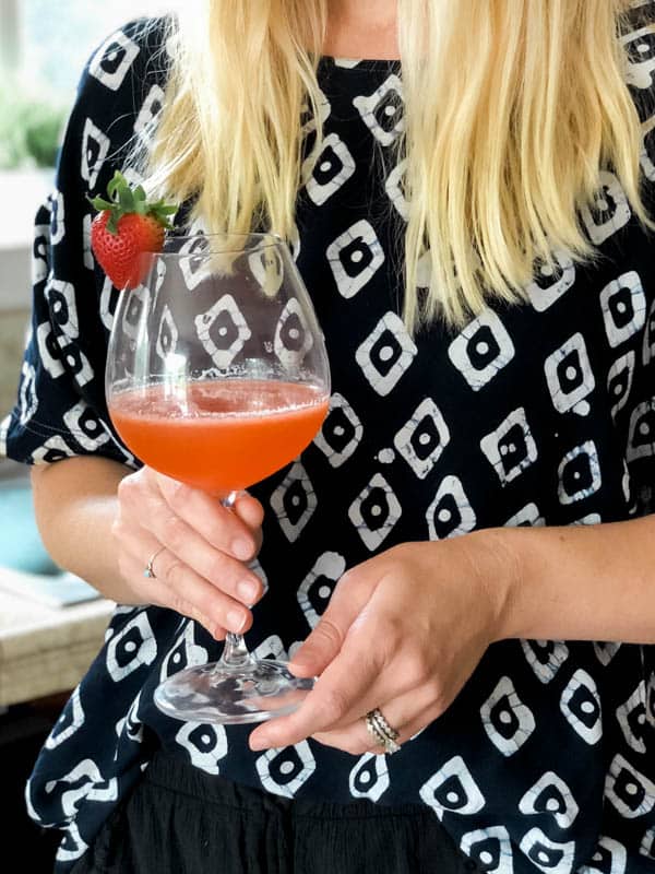 Woman holding a simple summer cocktail recipe with whiskey and strawberries in a wine glass.