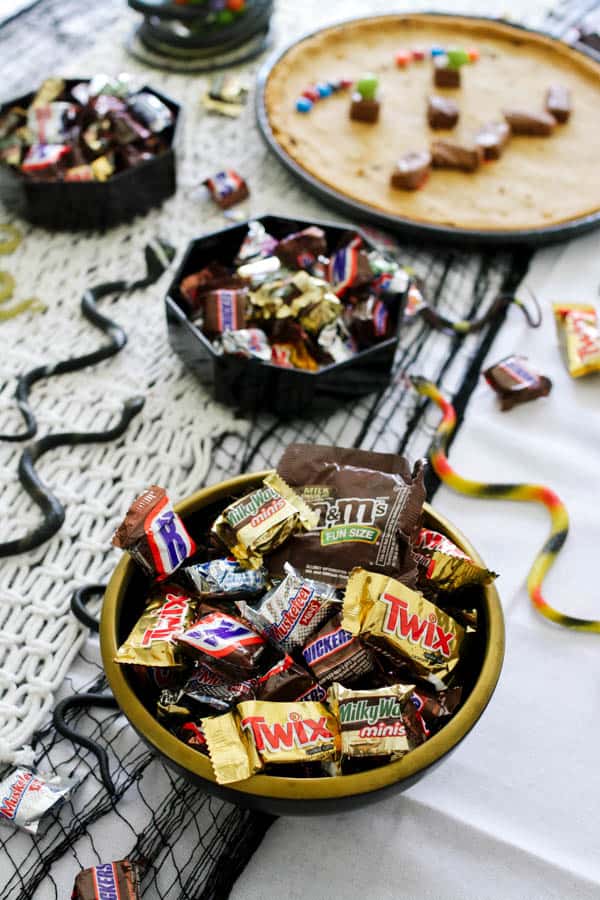 A bowl of fun-sized Halloween candy on a table with fake snakes for a kid's Halloween party. 