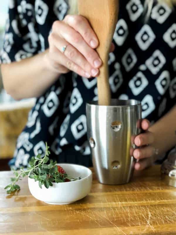 Woman using the back of a wooden spoon to muddle a cocktail.