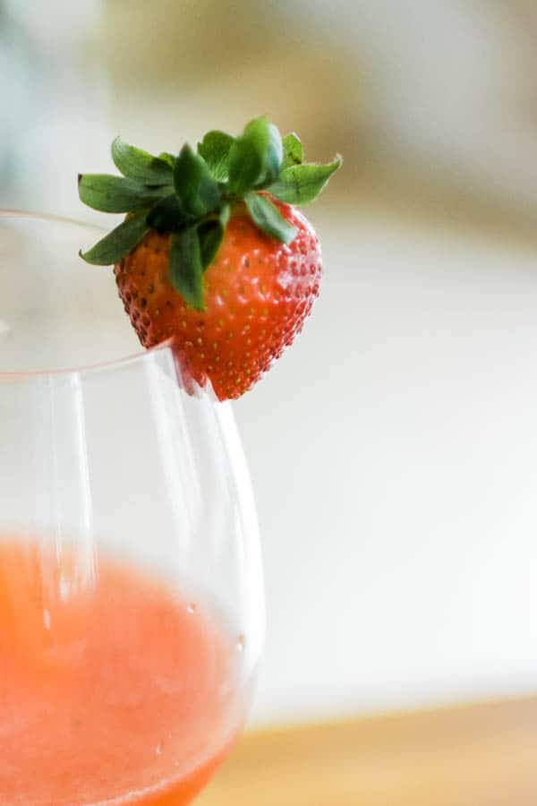 A strawberry split in the middle and sitting as garnish on the side of a wine glass.