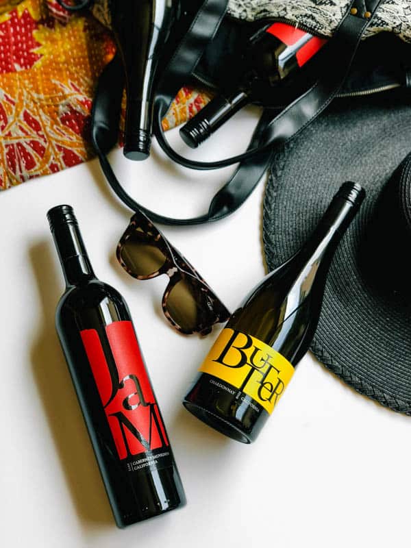 Two bottles of wine on a table next to a hat and sunglasses. 