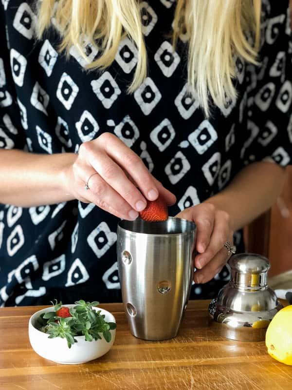 Woman adding a strawberry to a cocktail shaker.