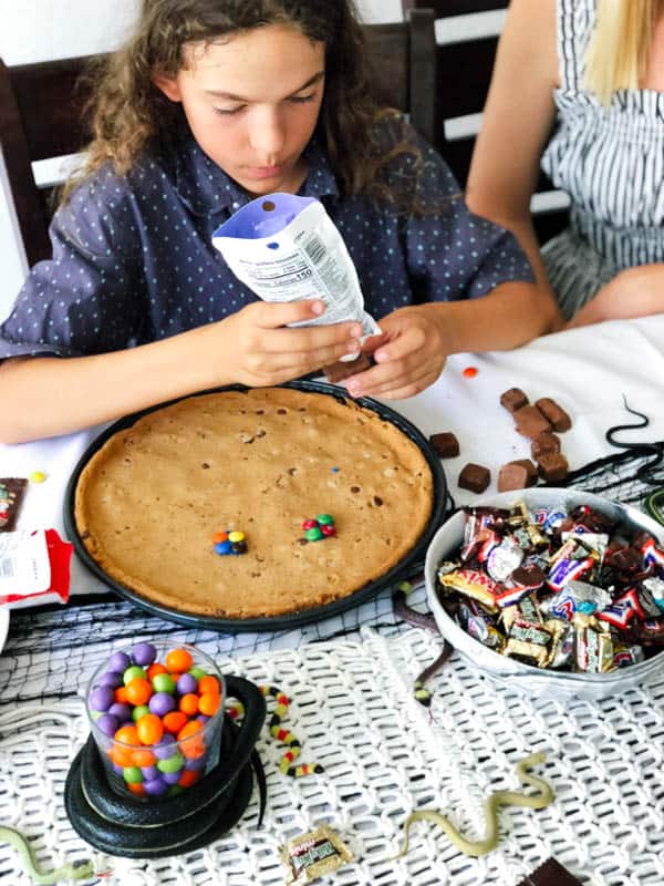 Kid decorating a giant cookie with candy to make a face. 