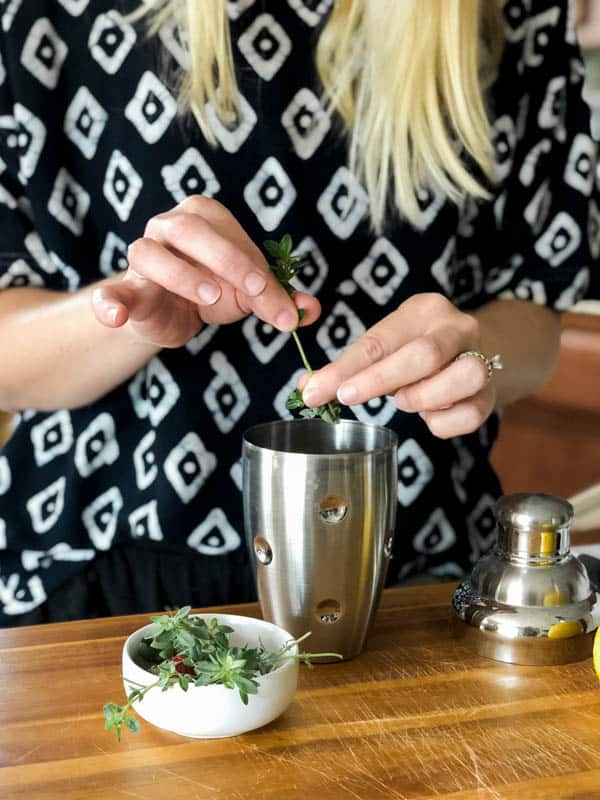 Woman adding fresh thyme to a cocktail shaker. 