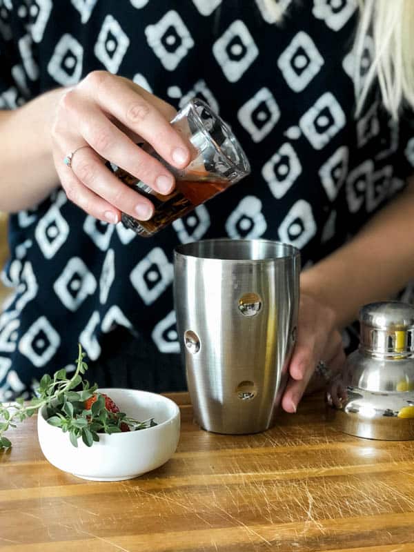 Woman adding a shot of Scotch to a cocktail shaker. 