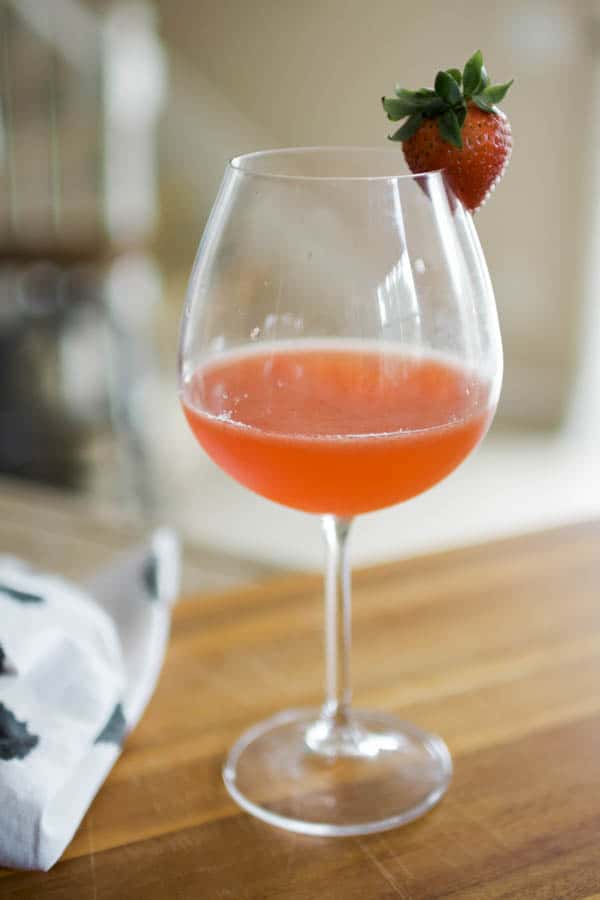 A strawberry whiskey sour served in a wine glass garnished with a fresh strawberry.