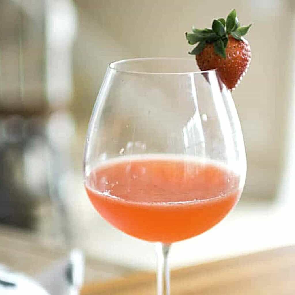Close up of a wine glass with a strawberry garnish and a strawberry whiskey sour in the glass.