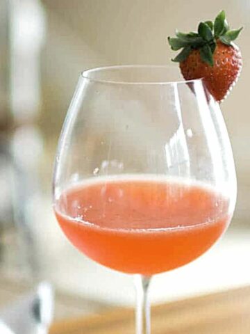 Close up of a wine glass with a strawberry garnish and a strawberry whiskey sour in the glass.