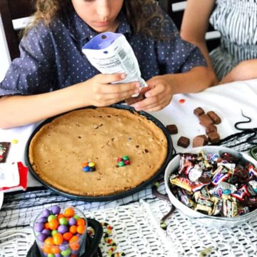 Boy writing on a giant cookie with frosting at a Halloween party table.