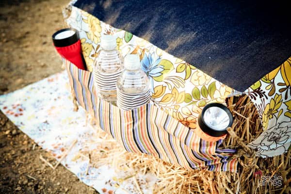 Close up of a hay bale covered in a fabric cover with pockets on the side holding flash lights and bottled water.