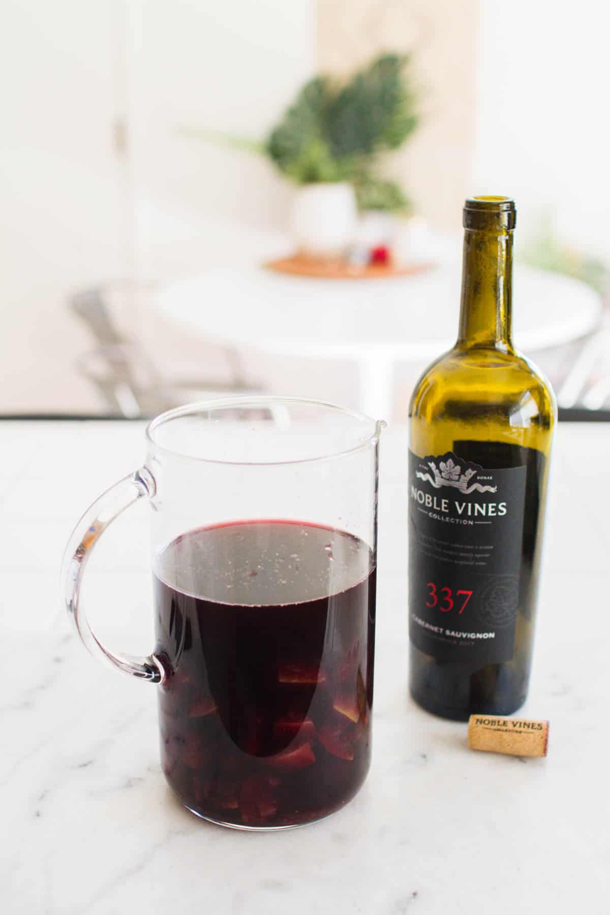 A pitcher of red wine and cooked apples next to an empty bottle of red wine.