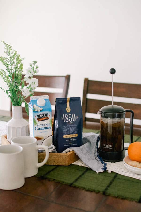 A tray of coffee and creamer on a table next to a French press.