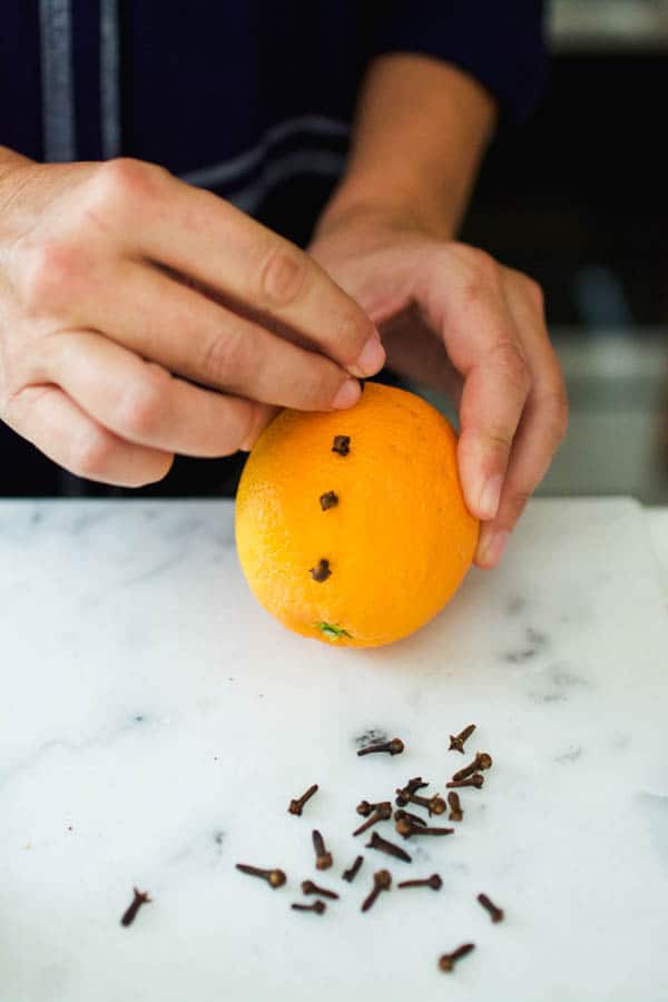 Hands studding cloves into an orange.