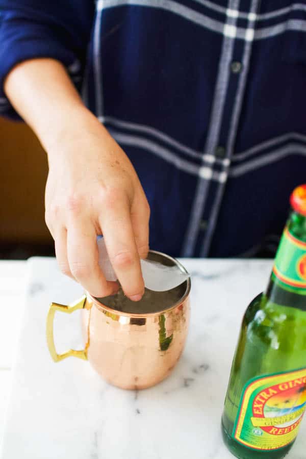 Woman putting ice cubes into a copper mug.