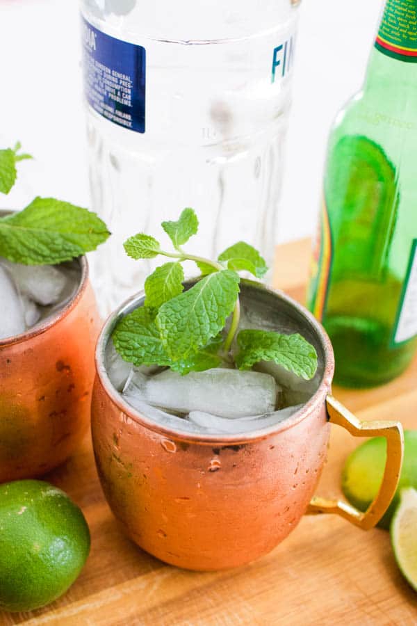 Moscow Mule in a copper mug garnished with fresh mint with the vodka and ginger beer bottles in the background.