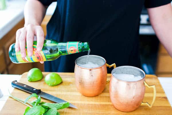 Topping off Moscow mules in copper mugs with ginger beer.