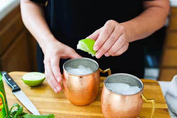 Squeezing fresh lime into copper mule mugs.