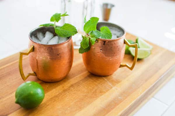 Pair of mule mugs garnished with mint on a cutting board.