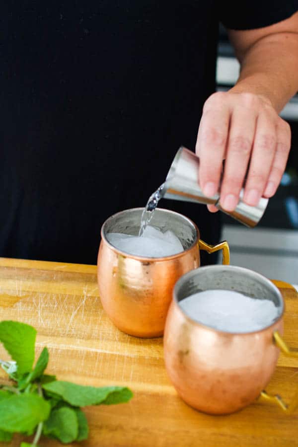 Making a Moscow Mule with vodka in copper mugs.