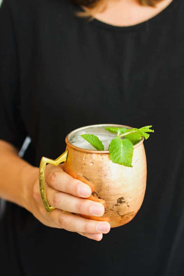 Original Moscow Mule recipe in a copper mug being held by a woman in a black top.