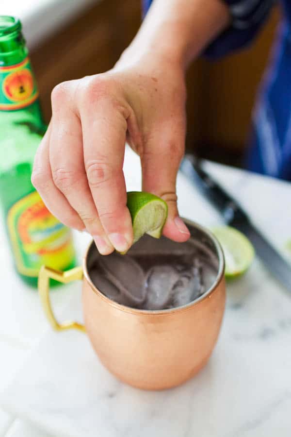Hand squeezing fresh lime into a copper mule mug.