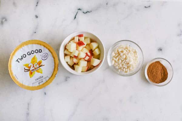 Vanilla yogurt next to a bowl holding apples, ginger pieces and cinnamon. 