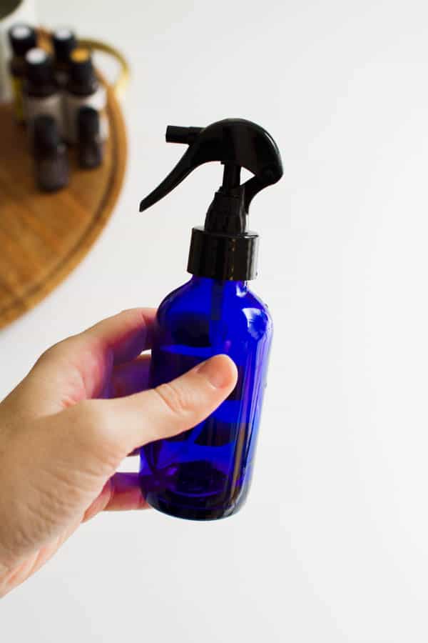 Woman holding a glass spray bottle with an essential oil room spray.