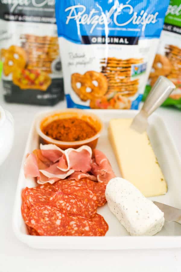 A charcuterie plate in front of a bag of Pretzel Crisps for a game day party.