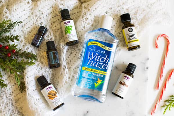 Witch hazel and a variety of essential oil bottles laying on a table next to candy canes and holiday greenery.