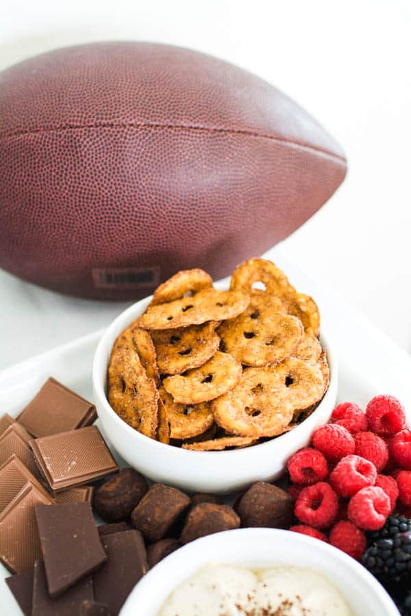 A football on a food table at a party next to dessert flavored Pretzel Crisps in a bowl and berries and chocolate next to it. 