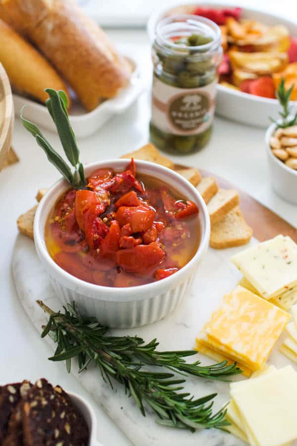 A roasted red pepper spread in a bowl next to cheese and other snacks on a table. 