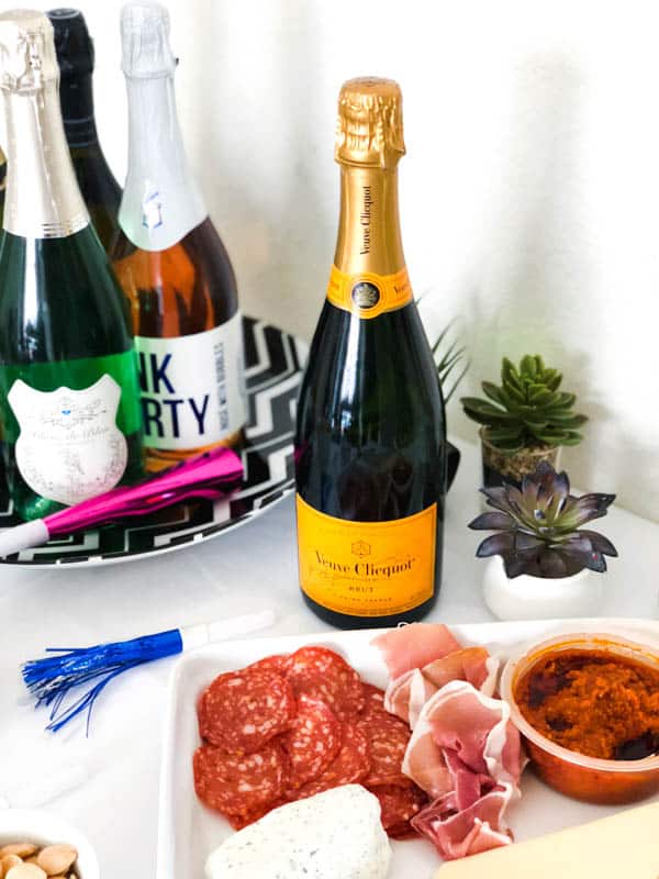 Close up of a bottle of Vueve Clicquot next to a charcuterie board and a tray of sparkling wine. 