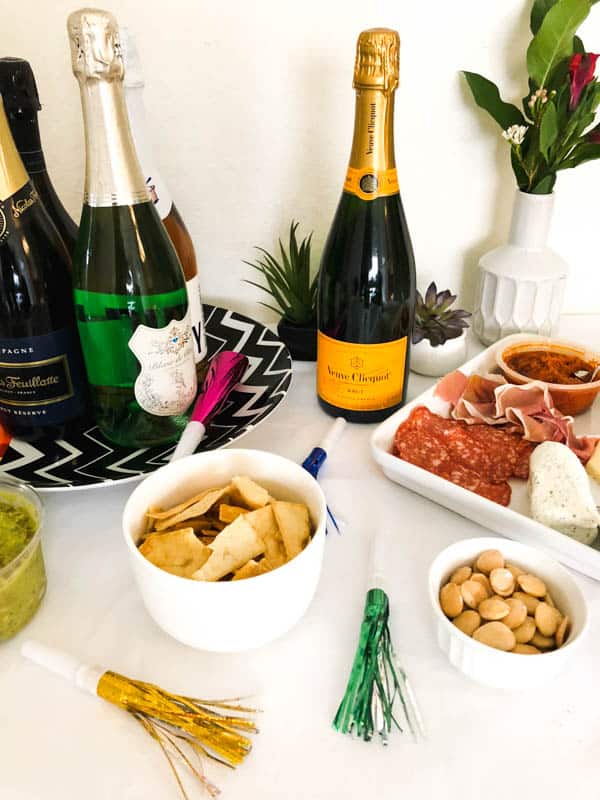 Noise blowers on a table with snacks and a charcuterie board next to a tray of sparkling wine.