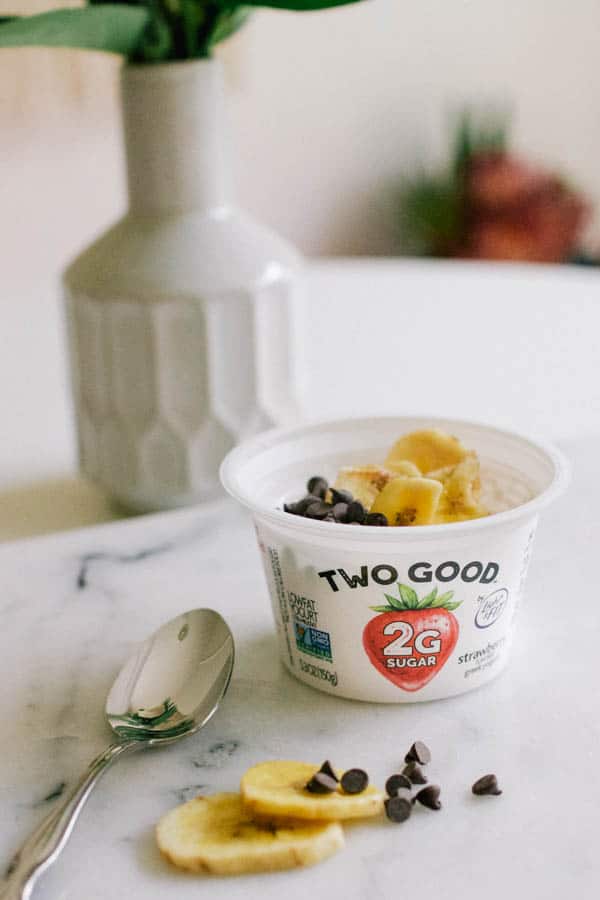 A small container of yogurt topped with mini chocolate chips and banana chips. 
