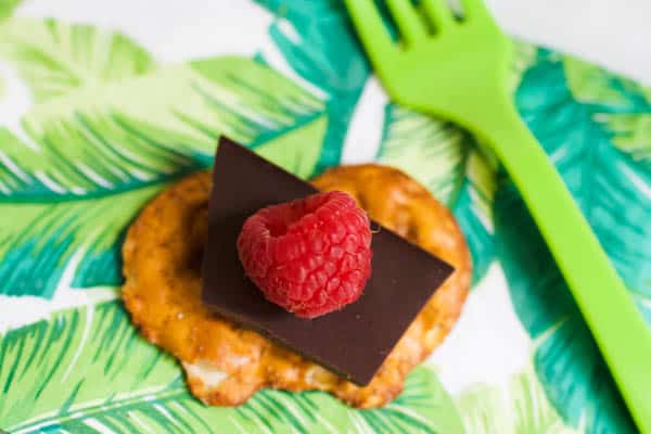 A Cinnamon Sugar Pretzel Crisp on a napkin topped with a piece of chocolate and a fresh raspberry. 