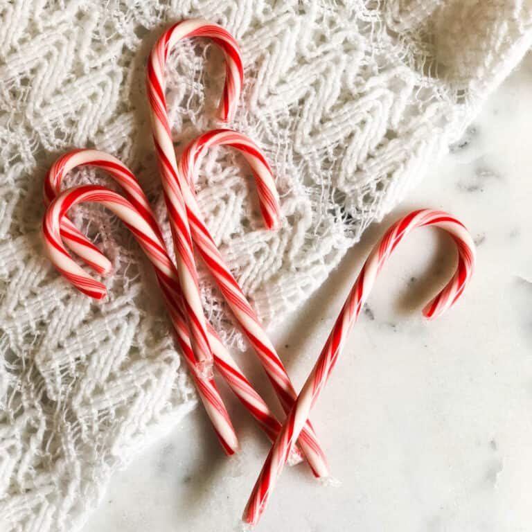 Square, top down image of candy canes on top of lace on a table.