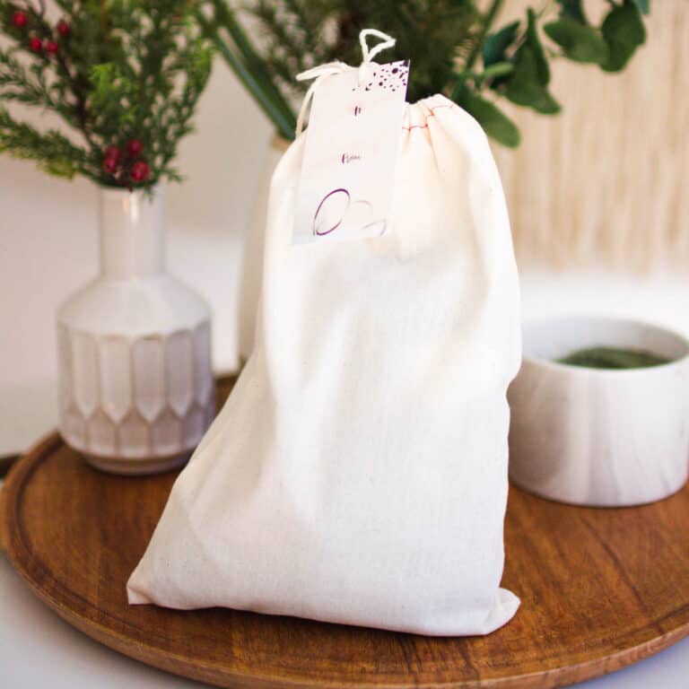 Small cloth bag on a wooden lazy susan, surrounded by small vases of greenery.