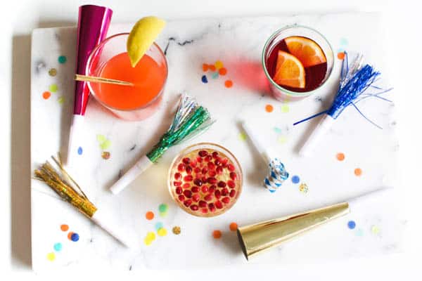 Non alcoholic drinks for New Year's Eve on top of a marble surface with noisemakers and confetti. 