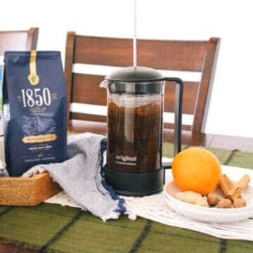 A French Press on a table with coffee next to a plate of spices.