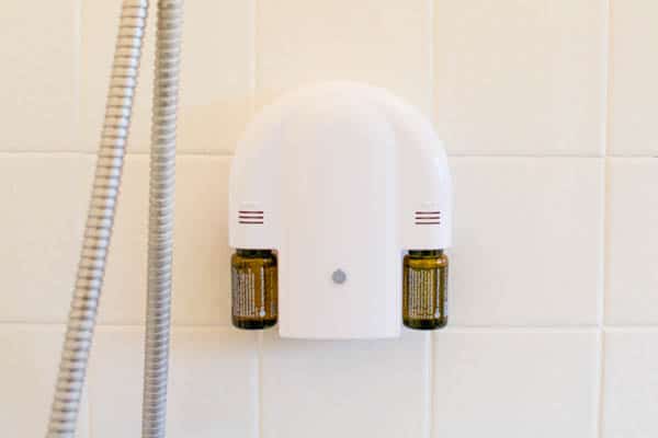 A waterproof shower diffuser with two bottles of essential oils installed on a shower wall. 