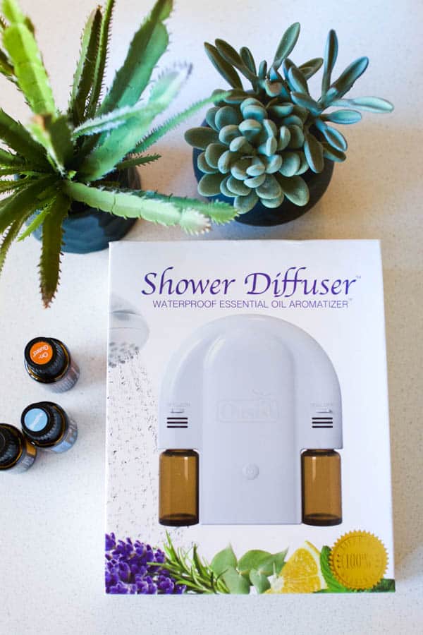 A Shower Diffuser in it's packaging laying on a table next to bottles of essential oils.