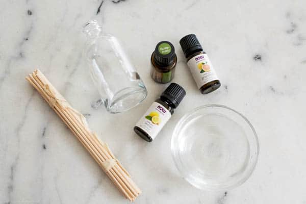 Overhead view of supplies to make a reed diffuser including essential oils, reeds and a glass bottle. 